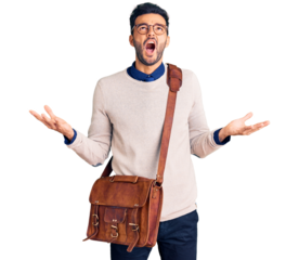 Young handsome hispanic man wearing leather bag crazy and mad shouting and yelling with aggressive expression and arms raised. frustration concept.