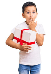 Little cute boy kid holding gift covering mouth with hand, shocked and afraid for mistake. surprised expression