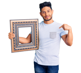 Handsome latin american young man holding empty frame pointing finger to one self smiling happy and proud
