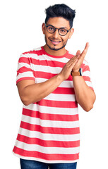 Naklejka premium Handsome latin american young man wearing casual clothes and glasses clapping and applauding happy and joyful, smiling proud hands together