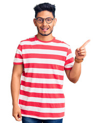 Handsome latin american young man wearing casual clothes and glasses with a big smile on face, pointing with hand finger to the side looking at the camera.