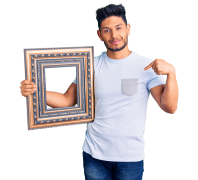 Handsome latin american young man holding empty frame pointing finger to one self smiling happy and proud
