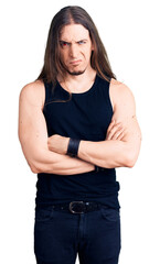 Young adult man with long hair wearing rocker style with black clothes and contact lenses skeptic and nervous, disapproving expression on face with crossed arms. negative person.