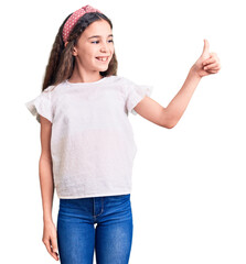 Cute hispanic child girl wearing casual white tshirt looking proud, smiling doing thumbs up gesture to the side