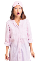 Young beautiful chinese girl wearing sleep mask and pajama afraid and shocked with surprise expression, fear and excited face.