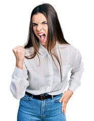 Young brunette teenager wearing business white shirt angry and mad raising fist frustrated and furious while shouting with anger. rage and aggressive concept.