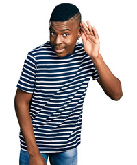 Young african american man wearing casual striped t shirt smiling with hand over ear listening and hearing to rumor or gossip. deafness concept.