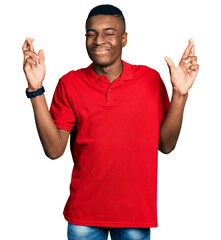 Young african american man wearing casual red t shirt gesturing finger crossed smiling with hope and eyes closed. luck and superstitious concept.