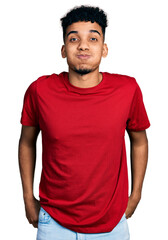 Young african american man wearing casual red t shirt puffing cheeks with funny face. mouth inflated with air, crazy expression. - obrazy, fototapety, plakaty