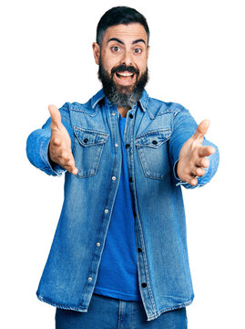 Hispanic man with beard with open arms doing hug gesture celebrating crazy and amazed for success with open eyes screaming excited.