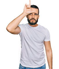 Fototapeta premium Young man with beard wearing casual white t shirt making fun of people with fingers on forehead doing loser gesture mocking and insulting.