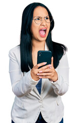 Beautiful hispanic woman with nose piercing using smartphone typing message angry and mad screaming...