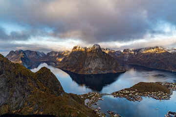 view from Reinebringen mountain over reine village with mountains reflected in water with golden color on lofoten islands in norway