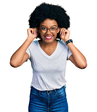 Young african american woman wearing casual white t shirt smiling pulling ears with fingers, funny gesture. audition problem