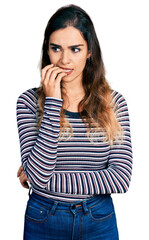Beautiful hispanic woman wearing casual striped shirt looking stressed and nervous with hands on mouth biting nails. anxiety problem.