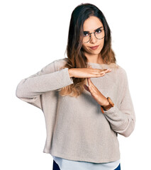 Beautiful hispanic woman wearing casual sweater and glasses doing time out gesture with hands,...