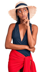 Young african american woman wearing swimsuit and summer hat with hand on chin thinking about question, pensive expression. smiling with thoughtful face. doubt concept.