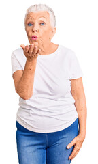 Senior beautiful woman with blue eyes and grey hair wearing casual white tshirt looking at the camera blowing a kiss with hand on air being lovely and sexy. love expression.