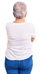Senior beautiful woman with blue eyes and grey hair wearing casual white tshirt standing backwards...