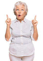 Senior grey-haired woman wearing casual clothes amazed and surprised looking up and pointing with...