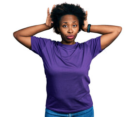 African american woman with afro hair wearing casual purple t shirt doing bunny ears gesture with...