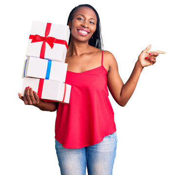 Young african american woman holding gift smiling happy pointing with hand and finger to the side