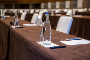 Empty convention center set up with tables, chairs, water, papers and pen for conference, business meeting, training course, lectures or seminars
