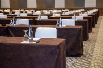 Empty convention center set up with tables, chairs, water, papers and pen for conference, business meeting, training course, lectures or seminars