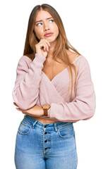 Beautiful blonde woman wearing casual winter pink sweater with hand on chin thinking about question, pensive expression. smiling with thoughtful face. doubt concept.