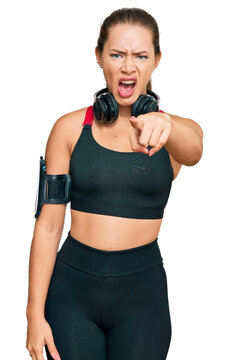Beautiful blonde woman wearing gym clothes and using headphones pointing displeased and frustrated to the camera, angry and furious with you