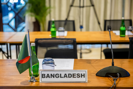 Name plate holder sign with Bangladesh flag, gooseneck paging microphone, notes and water on a table in conference hall during meeting, summit, forum or other event
