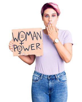 Young beautiful woman with pink hair holding woman power banner covering mouth with hand, shocked and afraid for mistake. surprised expression