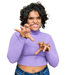 Young hispanic woman with curly hair wearing casual clothes smiling funny doing claw gesture as...