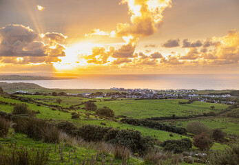 Golden Sunset with Sun Among the Clouds, Background Sea, and Green Meadow from the Top of a Hill