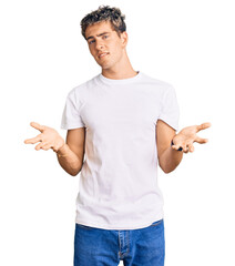 Young handsome man wearing casual white tshirt clueless and confused with open arms, no idea...