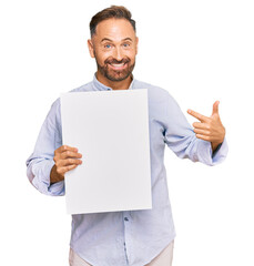 Handsome middle age man holding blank empty banner smiling happy pointing with hand and finger