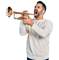 Young hispanic man with beard playing trumpet angry and mad screaming frustrated and furious, shouting with anger. rage and aggressive concept.