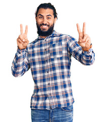 Young arab man wearing casual clothes smiling looking to the camera showing fingers doing victory...
