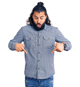 Young arab man wearing casual clothes pointing down with fingers showing advertisement, surprised face and open mouth