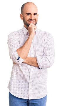 Young handsome man wearing elegant shirt looking confident at the camera with smile with crossed arms and hand raised on chin. thinking positive.