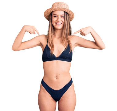Young beautiful girl wearing bikini and hat looking confident with smile on face, pointing oneself with fingers proud and happy.