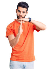 Young handsome man with beard wearing casual t-shirt doing time out gesture with hands, frustrated...
