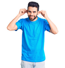 Young handsome man with beard wearing casual t-shirt smiling pulling ears with fingers, funny...