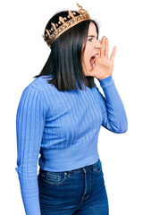 Young brunette woman with blue eyes wearing princess crown shouting and screaming loud to side with hand on mouth. communication concept. © Krakenimages.com