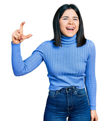 Young brunette woman with blue eyes doing size gesture holding invisible object smiling and laughing hard out loud because funny crazy joke.