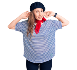 Young beautiful blonde woman wearing french beret and striped t-shirt smiling pulling ears with fingers, funny gesture. audition problem