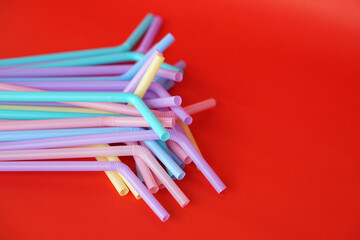 Colorful plastic drinking straws tubes for juice and cocktails, red background. Concept, single use equipment for drinking, but can use for diy crafts for decoration.     