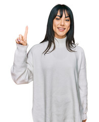 Young brunette woman with bangs wearing casual turtleneck sweater showing and pointing up with finger number one while smiling confident and happy.