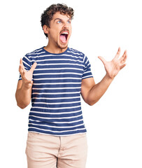Naklejka premium Young handsome man with curly hair wearing casual clothes crazy and mad shouting and yelling with aggressive expression and arms raised. frustration concept.