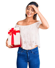 Young beautiful woman holding gift stressed and frustrated with hand on head, surprised and angry face